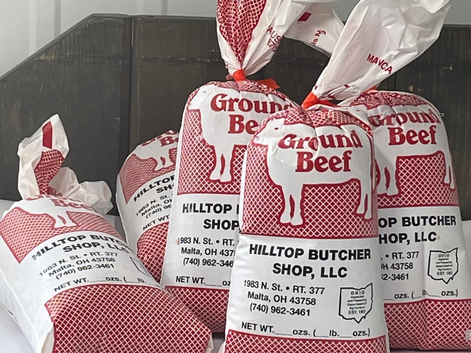 275466526_2722323481246630_2664532052441323376_n Bags of ground beef from Hilltop Butcher Shop, LLC, located in Malta, Ohio, showcasing red and white packaging with a cow graphic and product details.